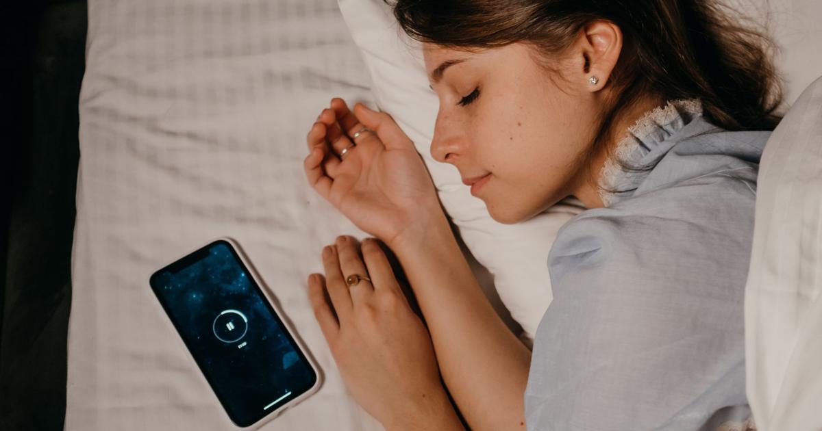 A nightstand at dusk with a sleep-tracking ring, a phone turned face-down, and a small notebook open to a simple two-week sleep log.